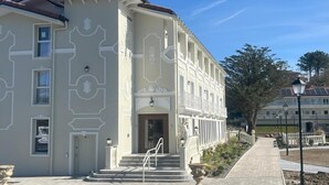 Un bâtiment à la façade symétrique, doté d’une entrée centrale avec des marches et d’un chemin piétonnier dallé.