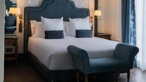 Un lit avec une tête de lit sombre, une literie blanche et deux oreillers. Il y a une chaise devant le lit.