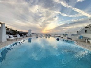 A pool with lounge chairs and a sunset view. - Ether Sunset Oia (Santorini)