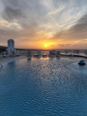 A pool area with lounge chairs and a view of the sunset over the water.