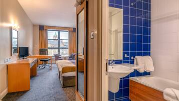 A hotel room with a bed, desk, chair, and a view of a cityscape.