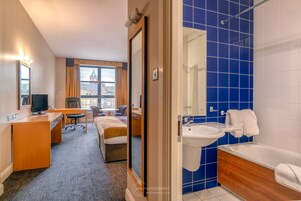 Habitación de hotel con cama, escritorio, silla y vista a un paisaje urbano.