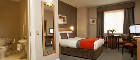 A hotel room with a bed, a desk, a chair, a television, a bathroom with a toilet and sink, and a mirror.