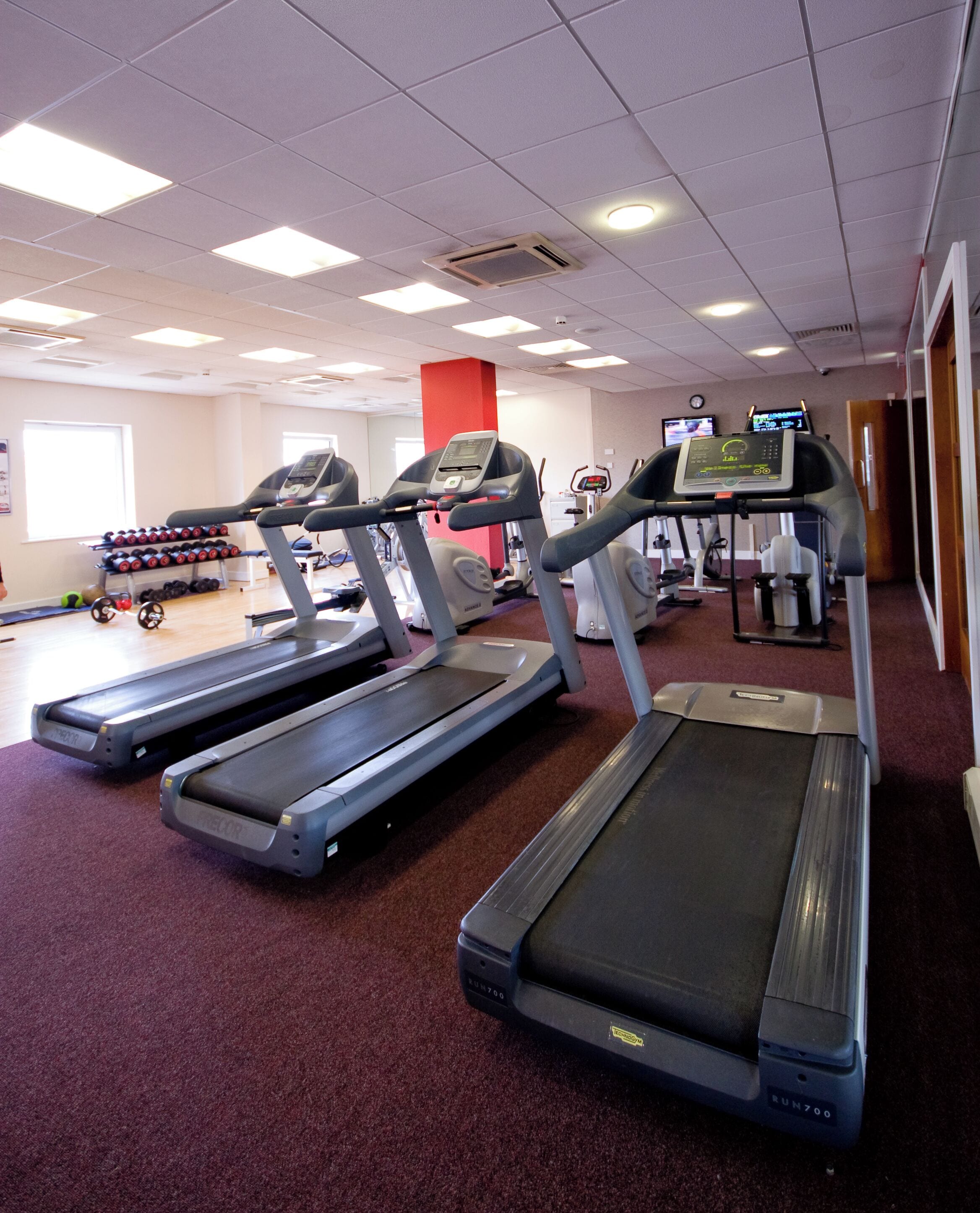 A gym with treadmills, weight machines, and a red pillar.