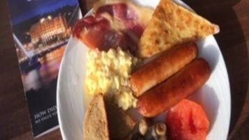 Een bord met roerei, worst, toast en champignons.