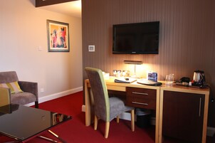 Habitación de hotel con escritorio, silla, televisión y alfombra roja.