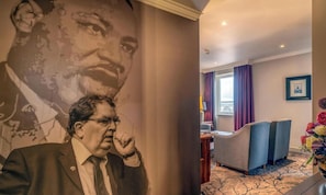 A hotel room with a large portrait on the wall, a seating area with a table, and a window with curtains. - City Hotel Derry (Londonderry)