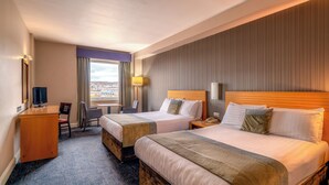 Quarto de hotel com duas camas, uma mesa, uma cadeira, uma televisão e uma janela com vista.