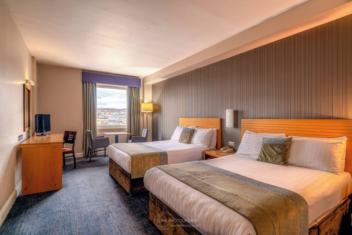 A hotel room with two beds, a desk, a chair, a TV, and a window with a view.