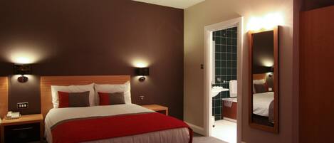 Une chambre d’hôtel avec un grand lit, des lampes de chevet, une table de chevet, un miroir et une porte donnant sur une salle de bain.