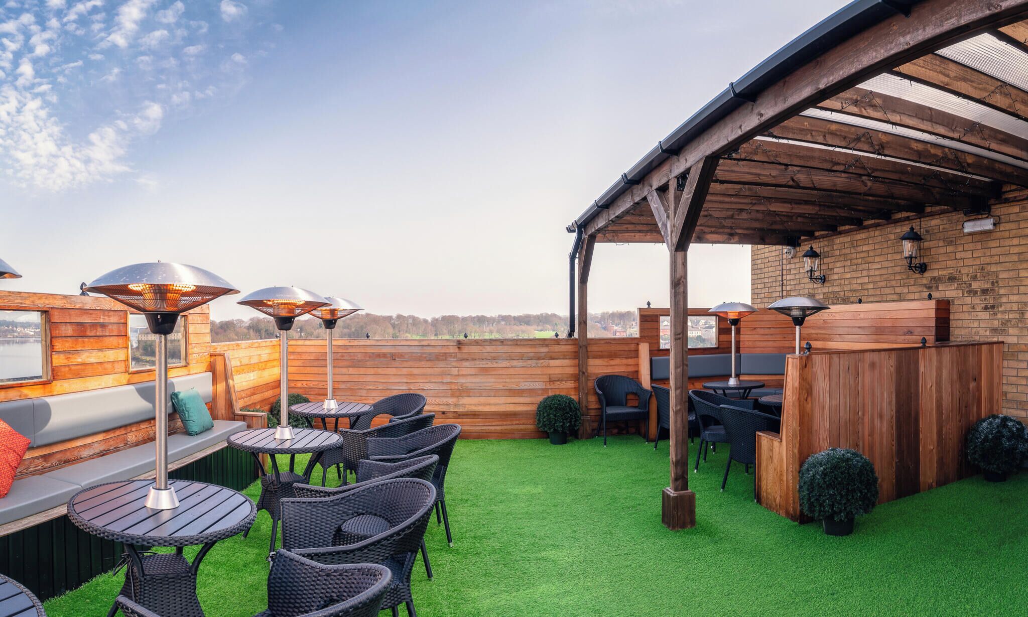 Eine Terrasse im Freien mit Holztischen und -stühlen, einem überdachten Sitzbereich und Blick auf die Landschaft.