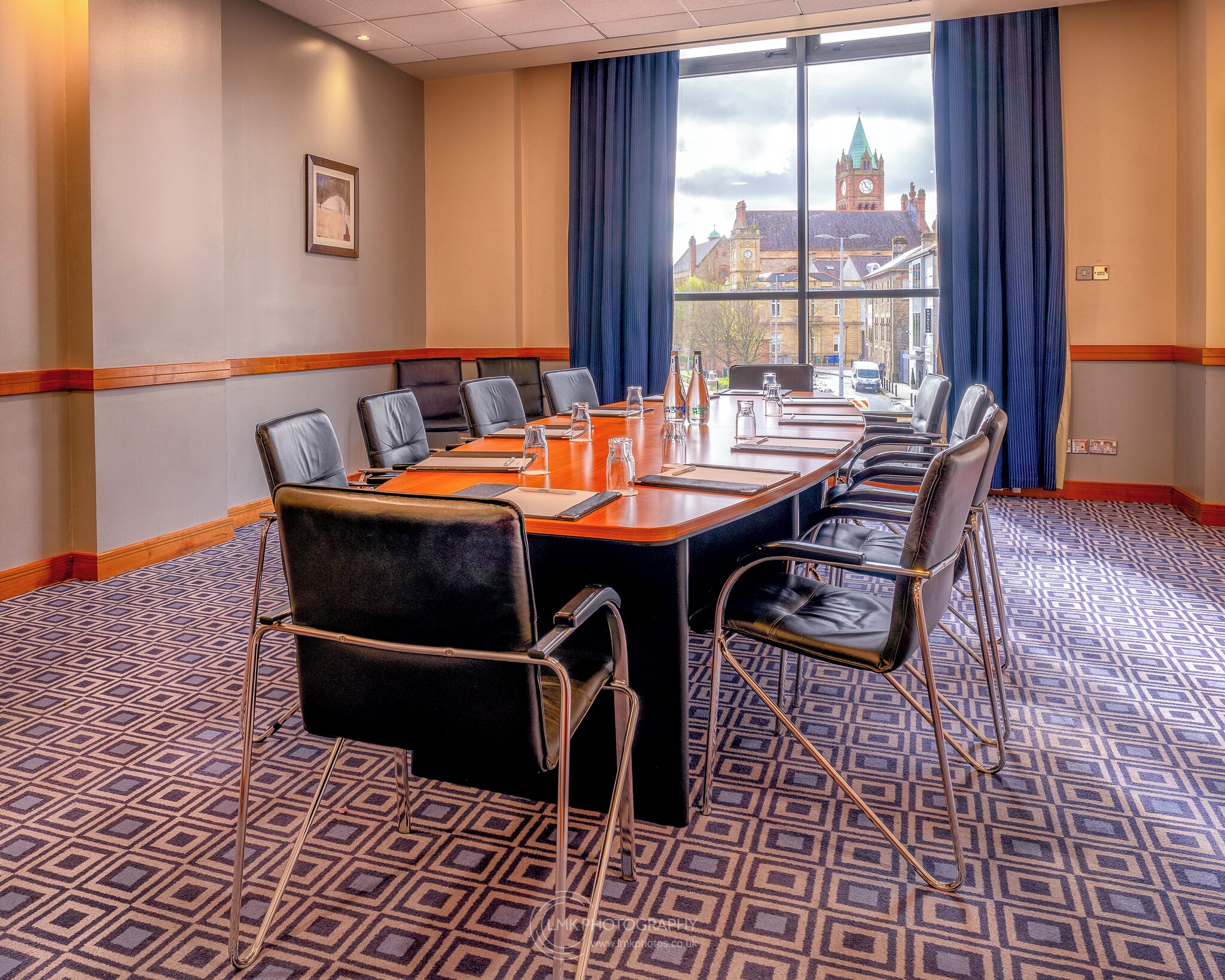 A conference room with a long table, black leather chairs, and a patterned carpet.