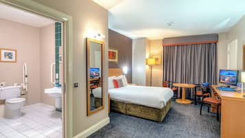 A hotel room with a bed, desk, chair, and a bathroom with a toilet and sink.