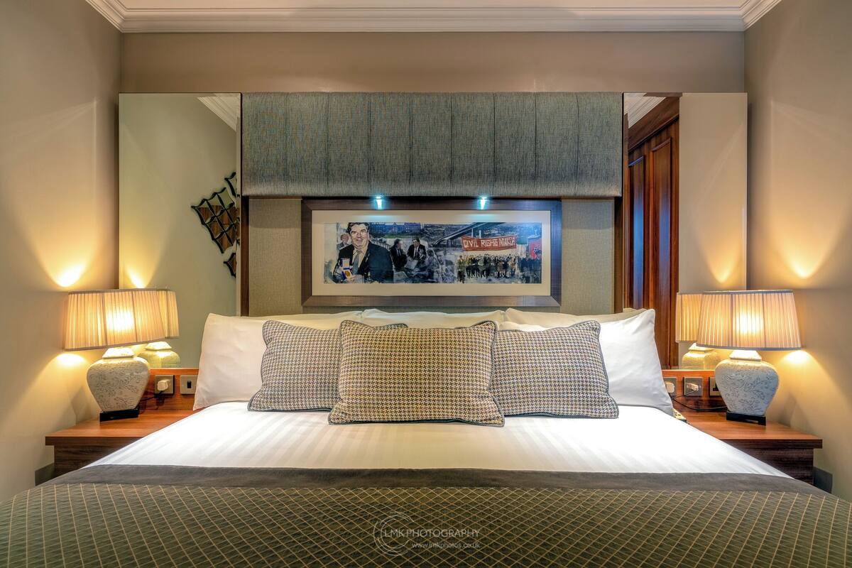 A neatly made bed with patterned pillows, two bedside lamps, and a framed picture above the bed.