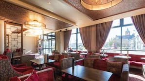 Um restaurante com assentos estofados vermelhos, teto estampado e grandes janelas com vista para a paisagem urbana.