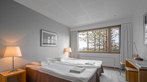 A modern hotel room with a large bed, a desk, and a window with a view of trees. - Hotel Pyhatunturi (Pyhätunturi)