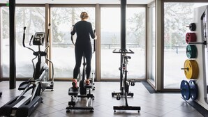 A gym with cardio machines, a weightlifting area, and large windows offering a snowy outdoor view. - Hotel Pyhatunturi (Pyhätunturi)