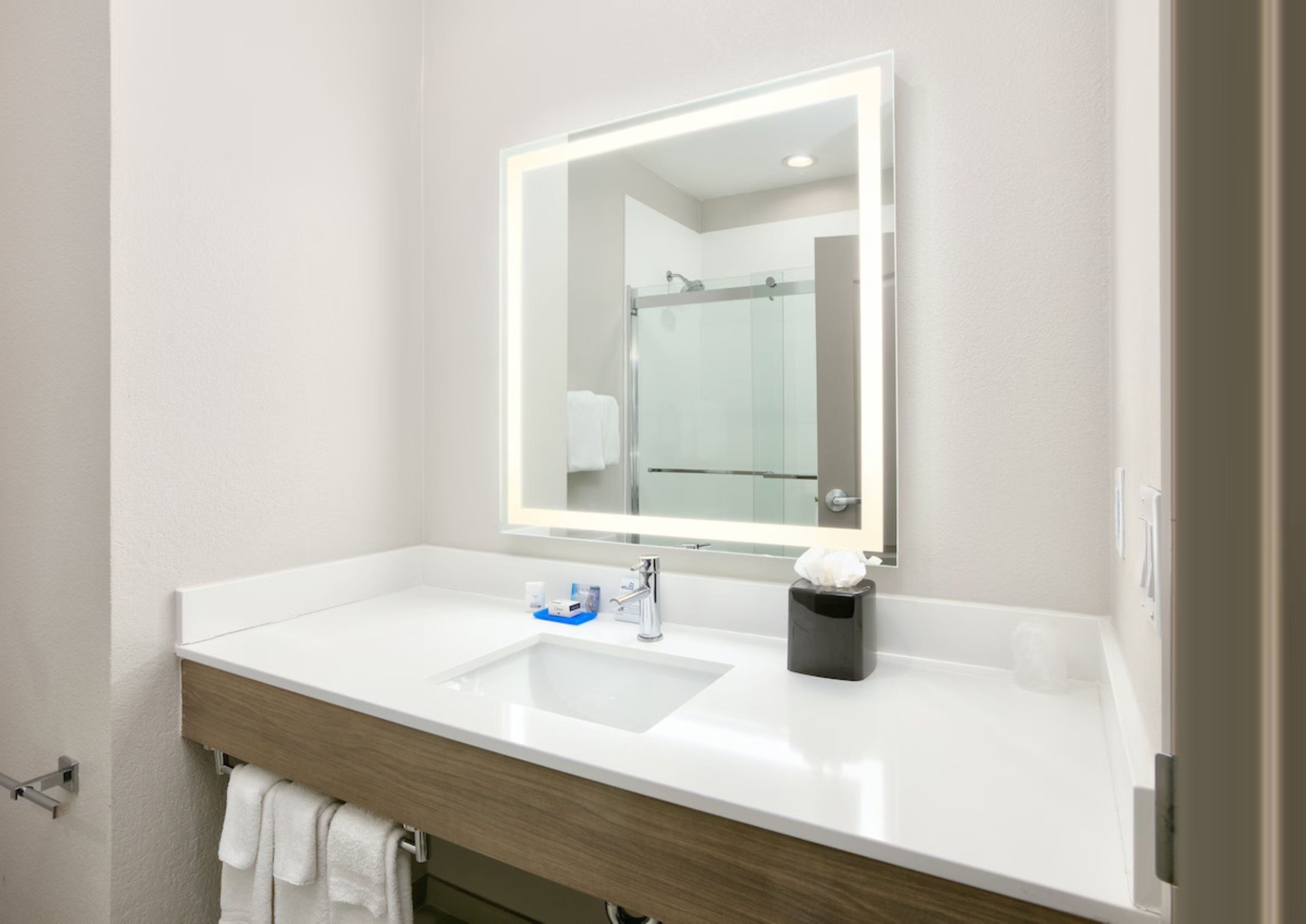 A modern bathroom with a white sink, a mirror with a light, and a towel rack.