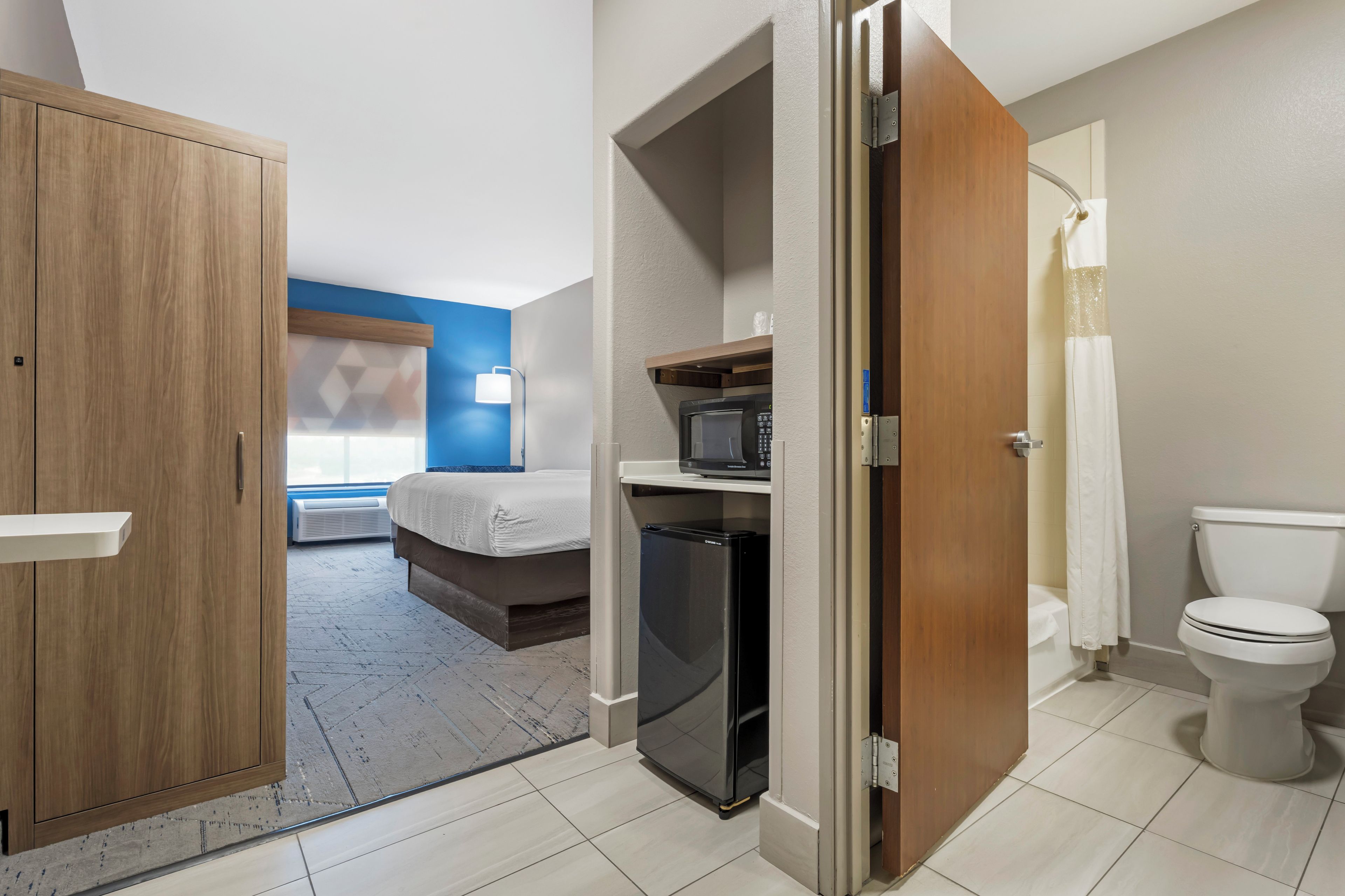 A hotel room with a bed, a microwave, a refrigerator, a toilet, and a wardrobe.