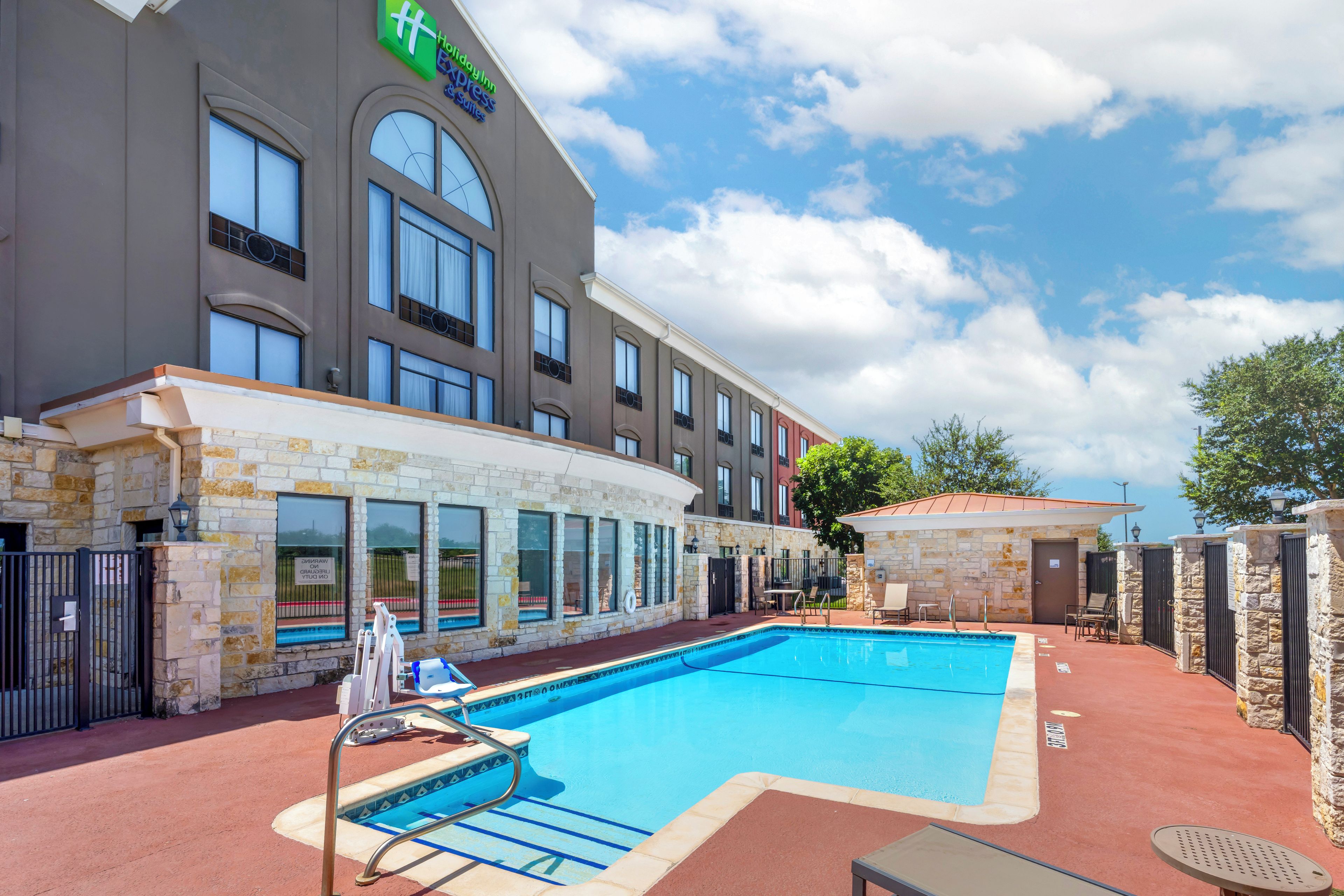 A hotel with a swimming pool, stone walls, and a clear sky.
