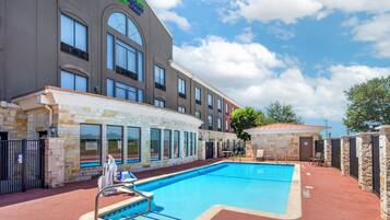 A hotel with a swimming pool, stone walls, and a clear sky.