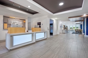 A hotel reception area with a modern design, including a reception desk, a digital display, and a vending machine.