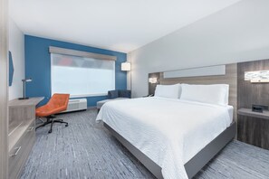A modern hotel room with a large bed, a desk, an orange chair, a window with blinds, and a nightstand with a lamp. - Holiday Inn Express Suites Beeville by IHG (Beeville)