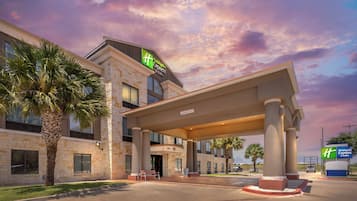 A Holiday Inn Express & Suites building with a stone facade, a covered entrance, and palm trees.