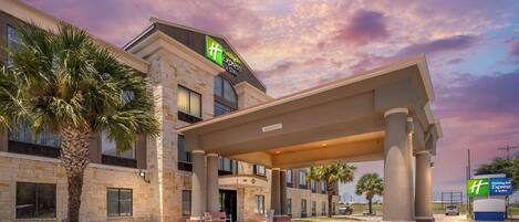 A Holiday Inn Express & Suites building with a stone facade, a covered entrance, and palm trees.