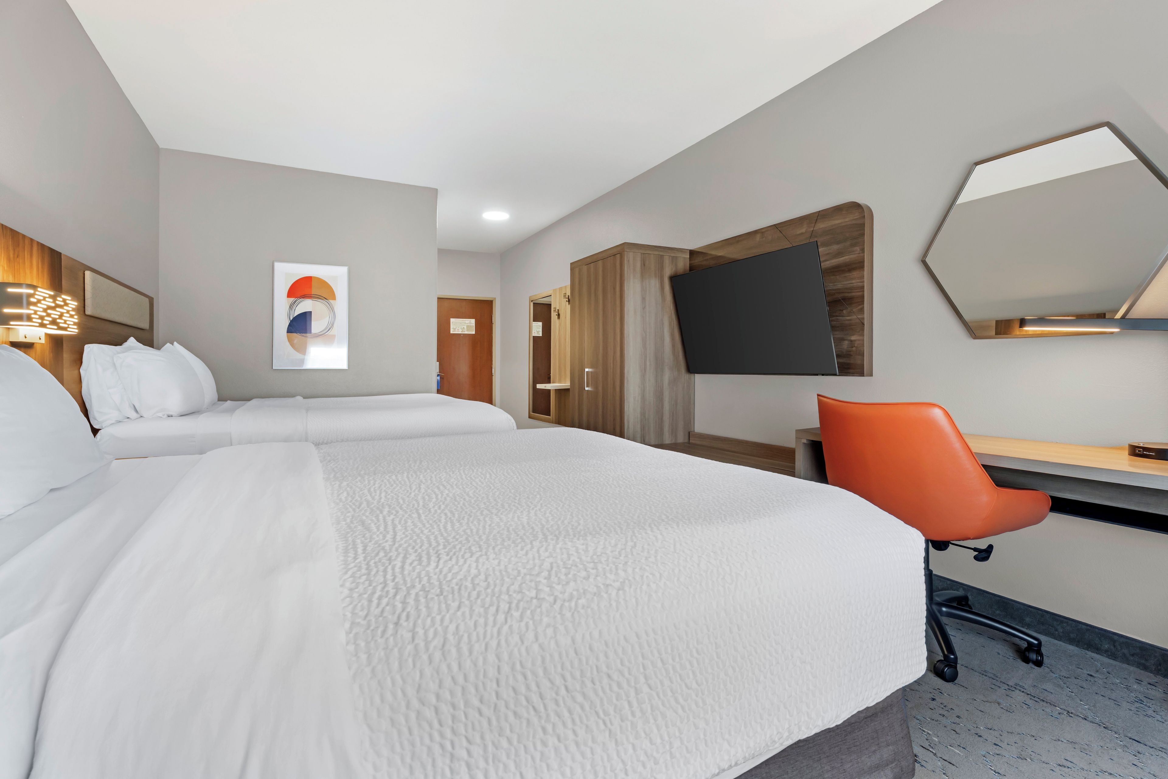 A hotel room with a bed, a desk, a chair, a flat-screen TV, and a mirror.