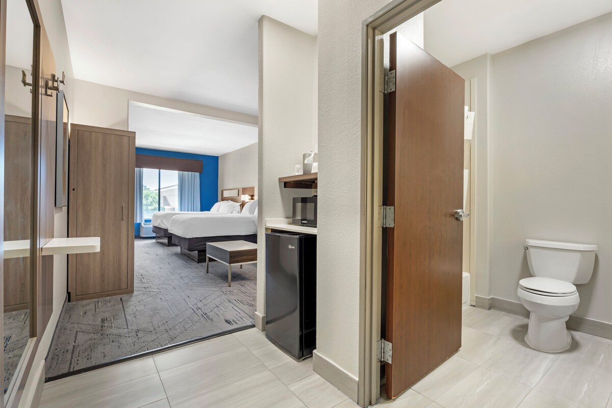 A hotel room with a bed, a desk, a refrigerator, and a toilet.