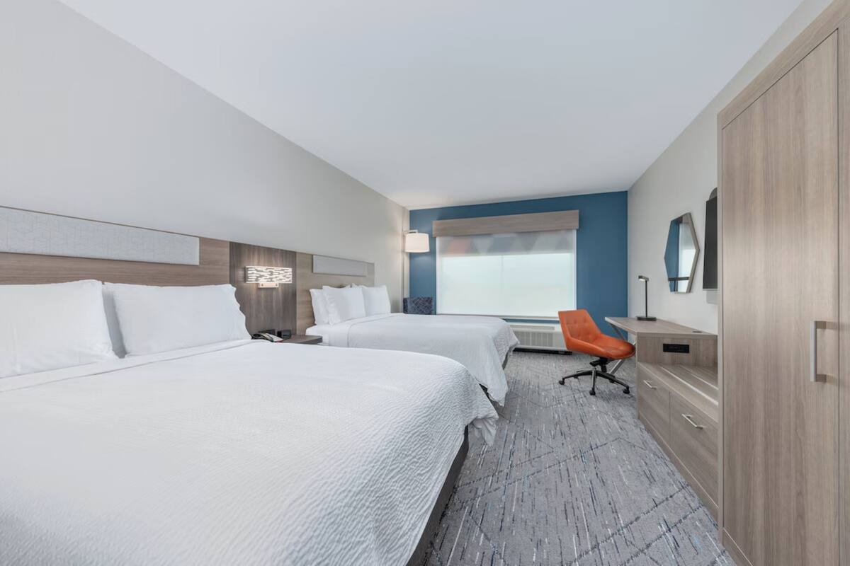 A hotel room with two beds, a desk, a chair, a wardrobe, and a large window with a view.