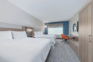 Habitación de hotel con dos camas, un escritorio, una silla, un armario y un ventanal con vistas.
