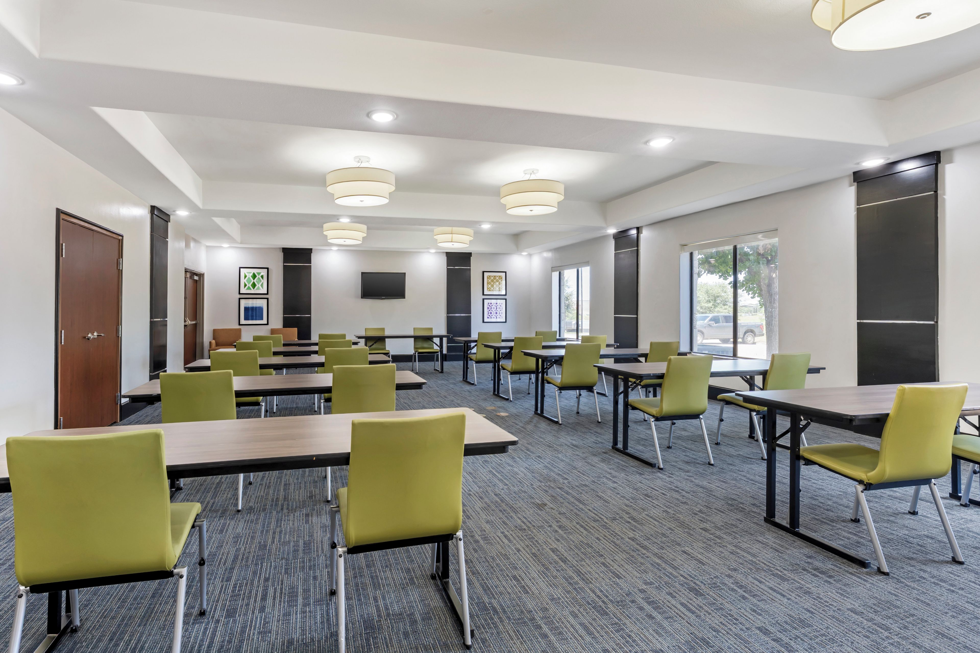 A conference room with multiple tables and chairs, a flat-screen TV, and framed artwork on the walls.