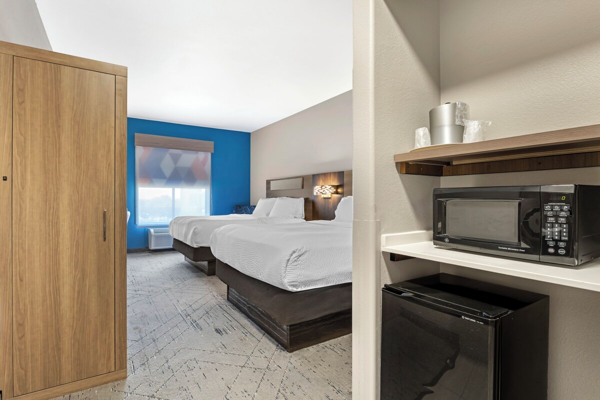A hotel room with a bed, a microwave, a small refrigerator, and a wooden wardrobe.