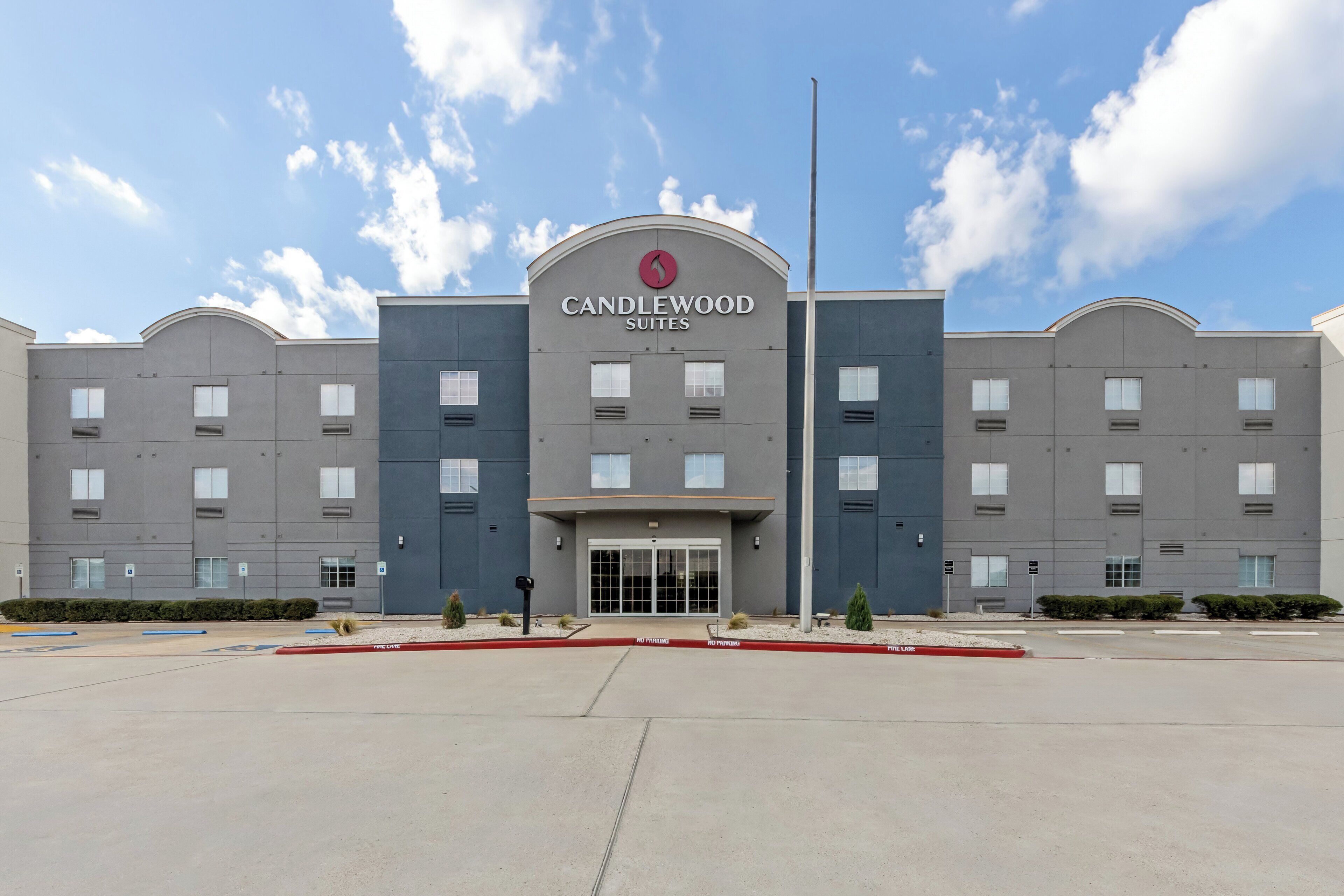 A multi-story hotel with a prominent entrance, a clear sky, and a parking lot in front.