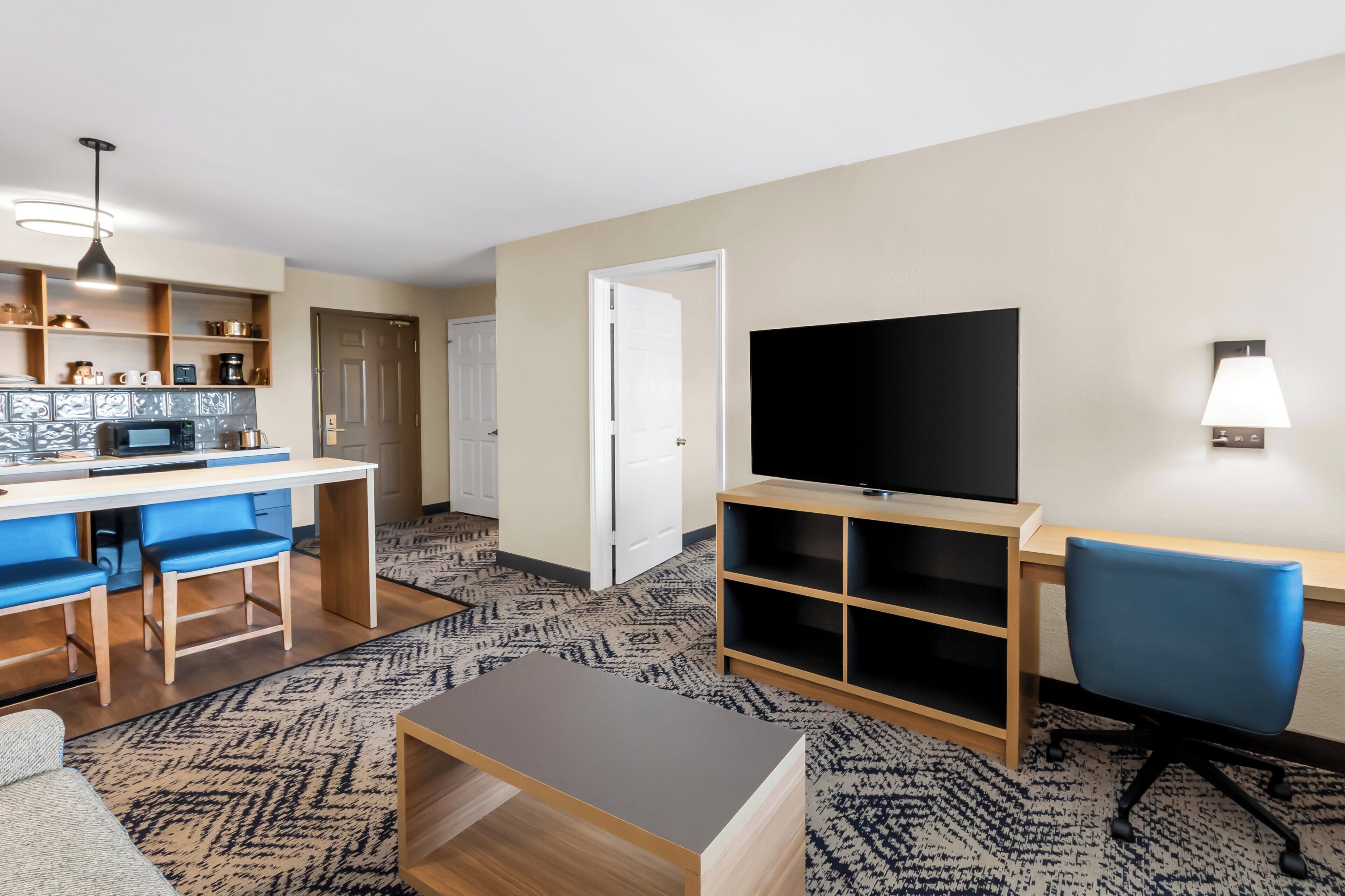 Een moderne woonkamer met een keukenhoek, een flatscreen televisie en een blauwe bureaustoel.