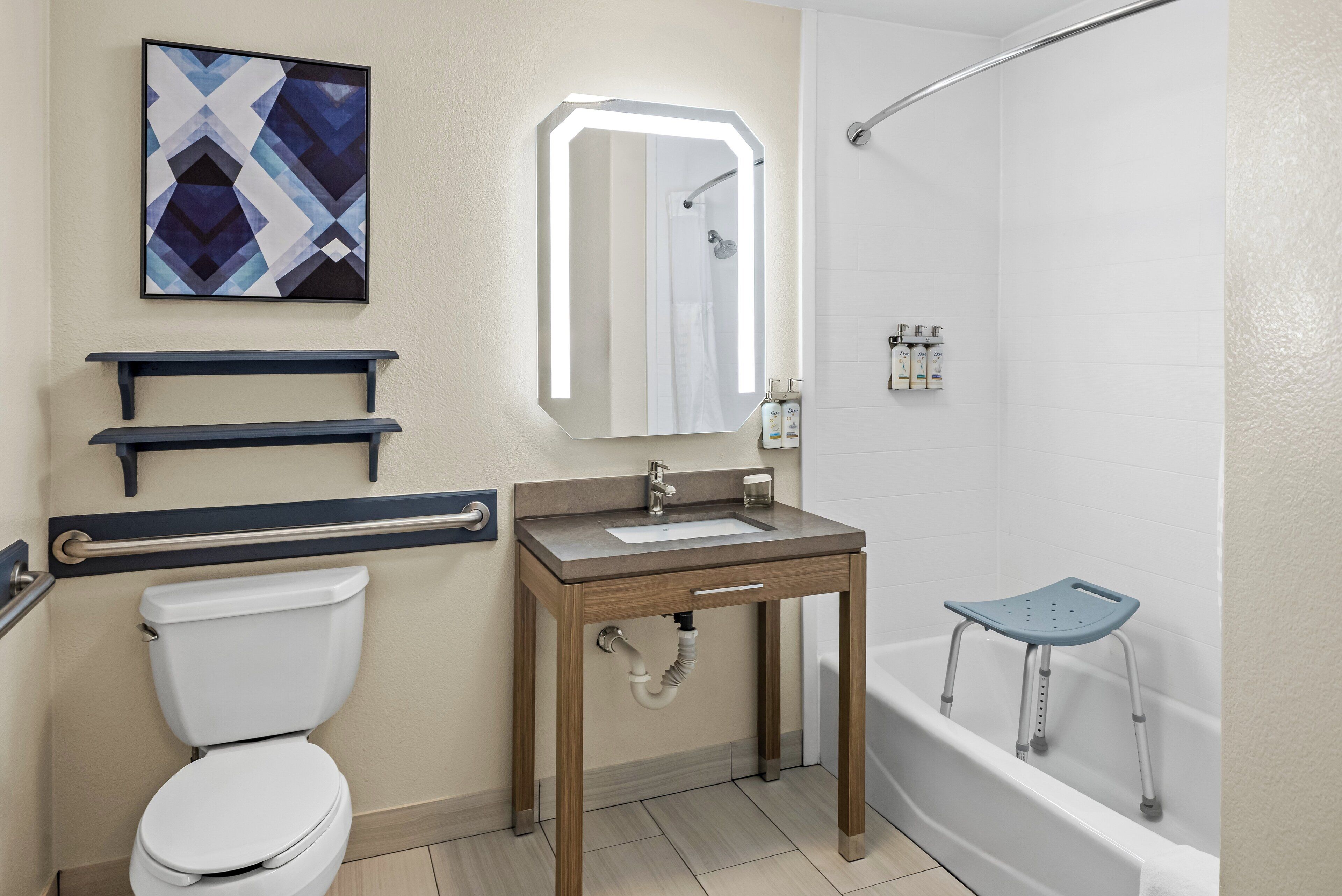 A bathroom with a toilet, sink, mirror, shower, and a grab bar.