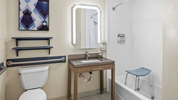 A bathroom with a toilet, sink, mirror, shower, and a grab bar.