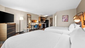 Habitación de hotel con dos camas, un escritorio, una silla, un televisor, kitchenette y baño.