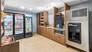 Interior moderno de una cafetería con máquinas expendedoras, una cafetera y un microondas.