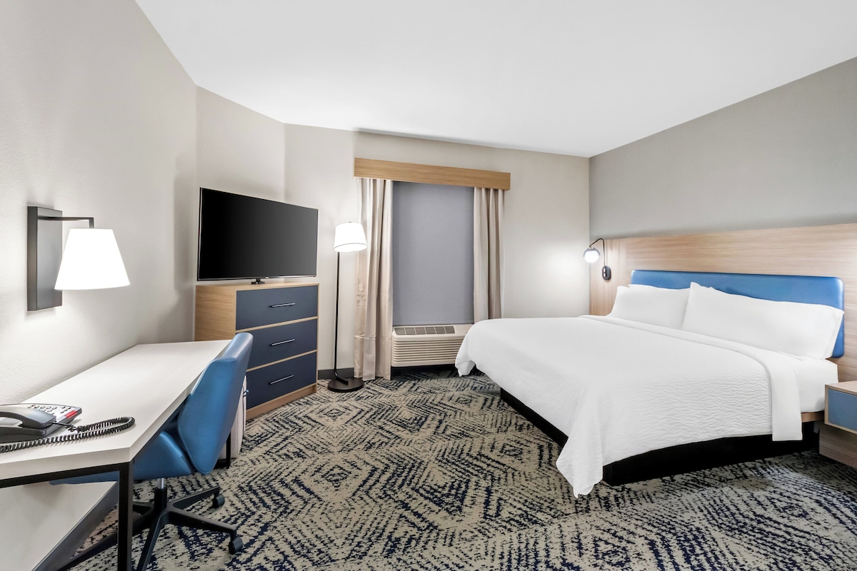 A hotel room with a bed, desk, chair, TV, and a window with curtains.