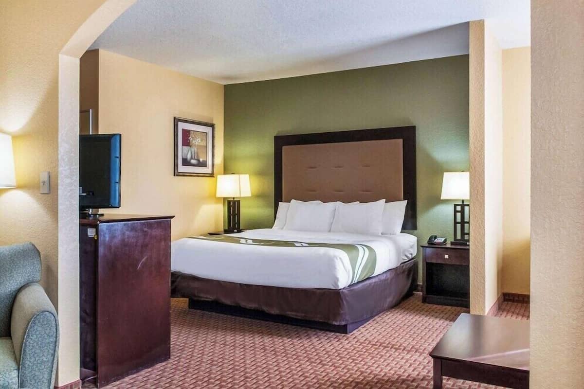 A hotel room with a bed, a desk, a chair, a television, and two bedside lamps.