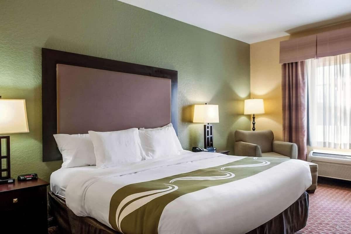 A hotel room with a large bed, two bedside lamps, a chair, and a window with curtains.