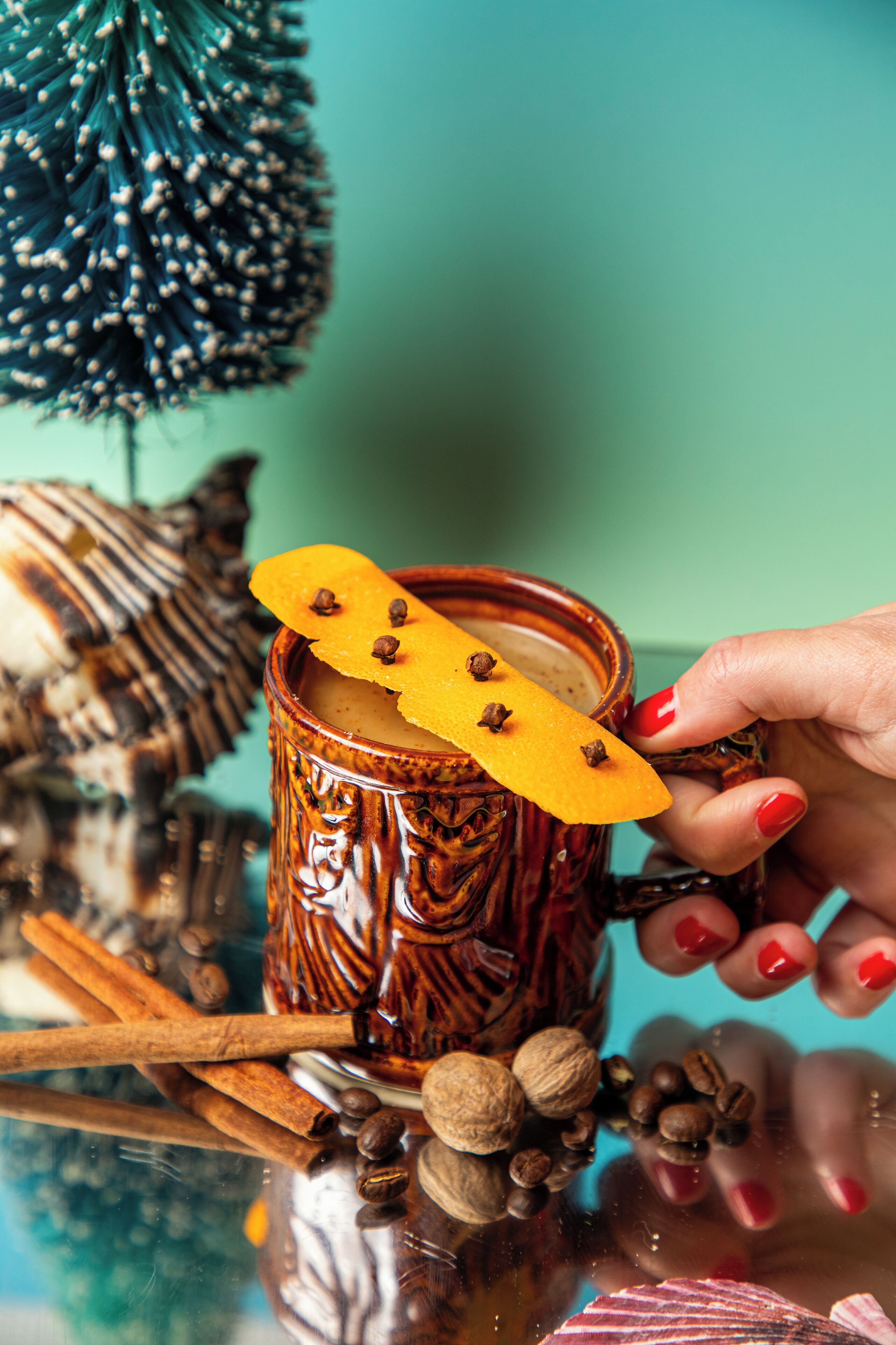 Une main tenant une tasse avec un bâton de cannelle et un croissant à la cannelle, entourée de grains de café et d’un biscuit rayé.