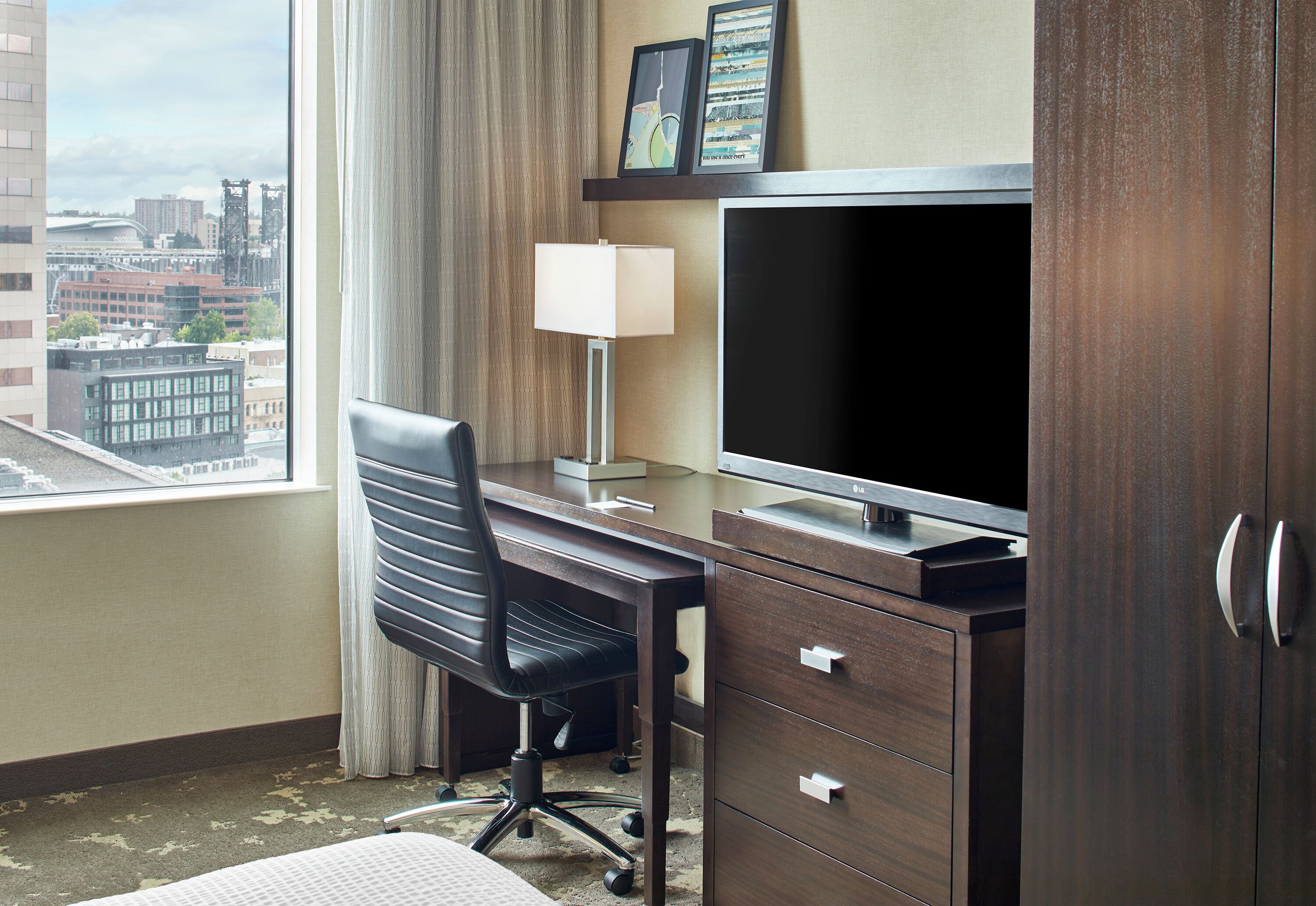 Habitación de hotel con escritorio, silla, televisión y vista a la ciudad.