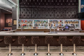 A bar area with a high, tufted headboard, multiple shelves of liquor bottles, and four bar stools. - Courtyard by Marriott Portland City Center (Portland)