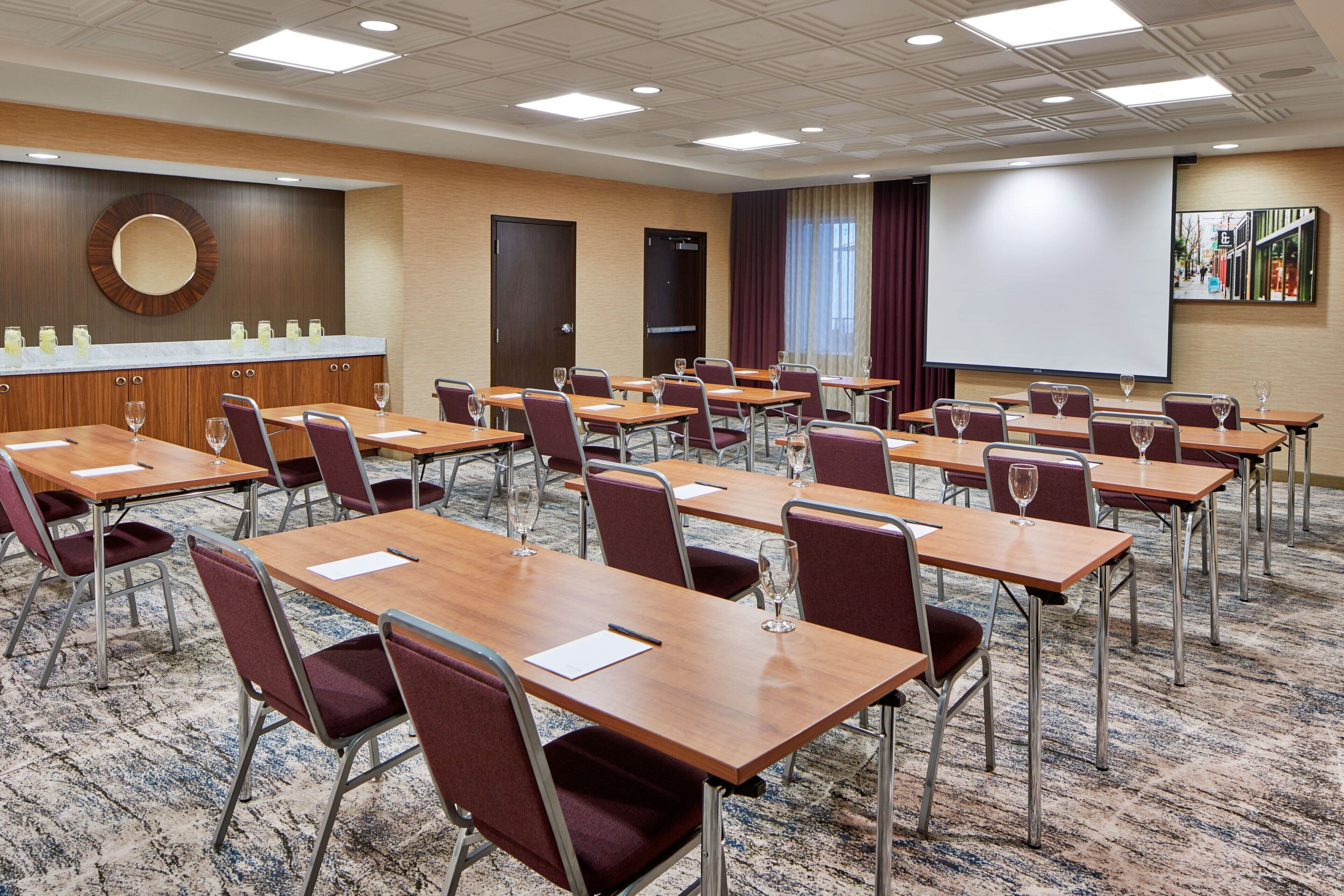 A conference room with multiple tables and chairs, a large screen, and a projection screen.