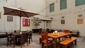 A spacious indoor dining area with a wooden table and chairs, two large umbrellas, and string lights. - Courtyard by Marriott Portland City Center (Portland)