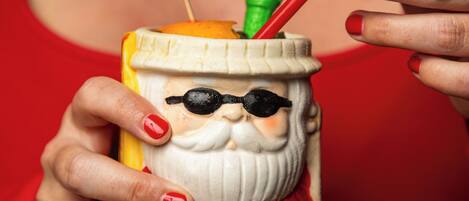 A person holding a ceramic mug with a Santa Claus design, featuring a straw and a small umbrella.